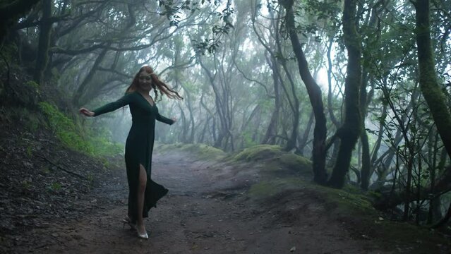 Beautiful woman in an elf costume is walking in a magic green enchanted forest.