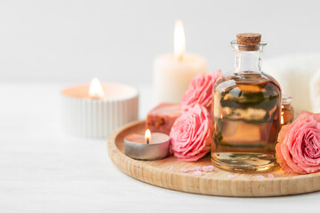 Aromatherapy. Concept of pure organic essential rose oil. Elixir with plant based floral or herbal ingredients. Pink flowers extract. Spa atmosphere with candle, towel. White background