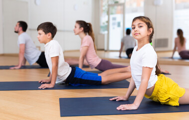 Girl looking at camera while doing cobra pose with her brother and parents on yoga family training.