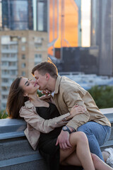 Young happy beautiful loving couple on a surprise romantic date on a rooftop on a Saint Valentine's Day. Attractive man and woman, male and female hugging, kissing. Sunset, skyscrapers urban view