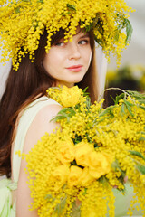 beautiful gentle young woman brunette with a bouquet and in a wreath of mimosa