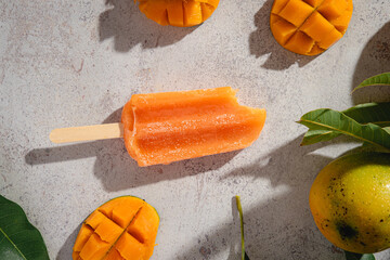 primer plano de paleta de helado de mango en un fondo rustico con espacio para copy y hojas de mango y fruta tropical