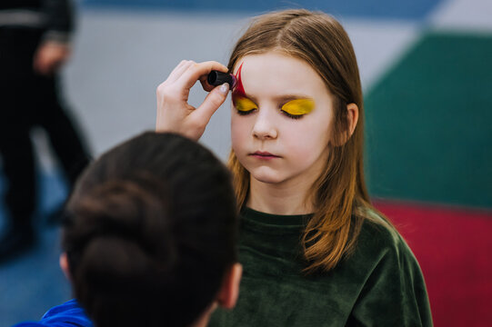 A professional make-up artist, artist paints with a brush on her face with face paints, drawing, children's makeup for a little girl model, a child. Photography, art, concept, lifestyle.