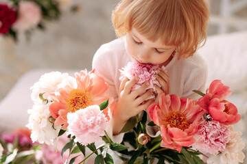 Child Blonde 6-7 years old in a white dress holds pale pink flowers in her hand. The concept of...