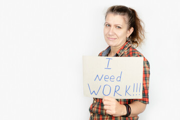 A middle-aged woman holds a sign in front of her with the inscription - I need a job, the woman lost her job, now she is looking for a new one. The woman is positive and smiling
