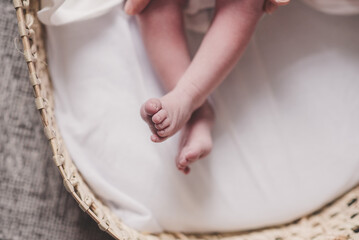 Close up of a baby's feet and lower legs in a moses basket on white sheets
