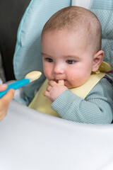 Close-up shot of a baby sucking its thumb while eating baby food