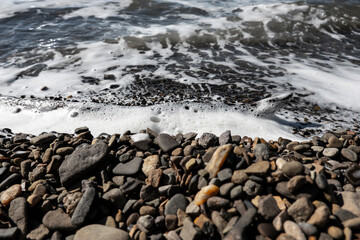 Tidal sea waves with foam on a gravel beach