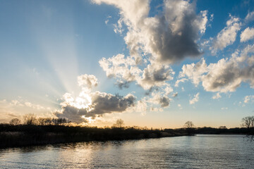 Fototapeta na wymiar Sky with bright sun behind clouds with sun rays with reflection in a lake