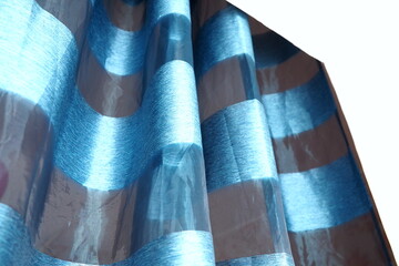Satin curtains, blue striped tulle hanging over the window. Edge of a white wall. Beautiful silky...