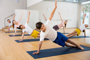 Naklejka na ściany i meble Boy exercising side plank on mat during family training in gym.