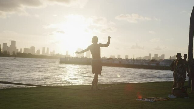 Slow motion silhouette of young man on slackline in park in Miami Florida at sunset