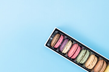 Seven macaroons in a box on blue.