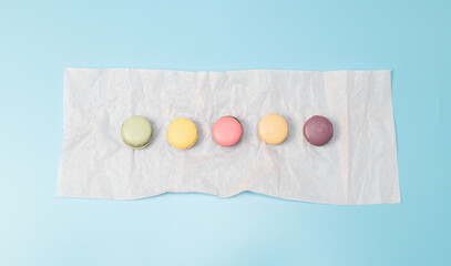 Five macaroons on a pale pink napkin on a blue background.