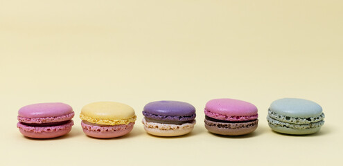 Five colorful macaroons on a yellow background.