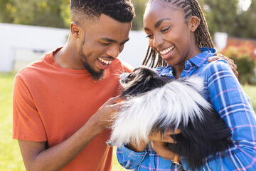 Happy african american couple playing with their pet dog in garden