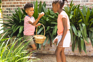 Happy african american children playing egg hunt in garden at easter
