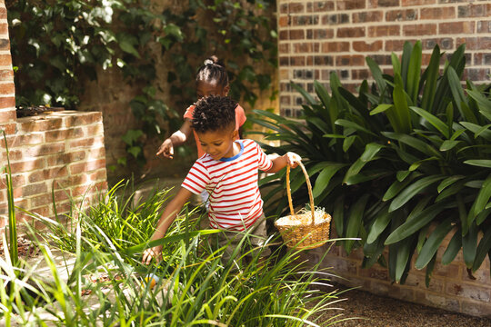 Happy african american children playing egg hunt in garden at easter