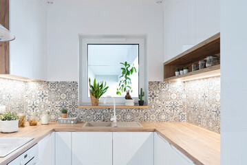 Modern kitchen with white furniture, wooden counter top, tiles pattern and sink near the window....