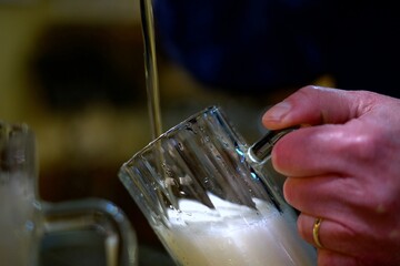 Detail of a mug of draft pils beer with white foam as it is poured from the brewmaster's hand                    