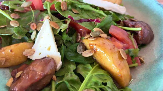 salad with liver and pear Warm autumn salad chard leaves, chicken liver, caramelized pear an mix, caramelized chicken liver with apples, couscous, raspberry sauce, pumpkin seeds on a blue plate