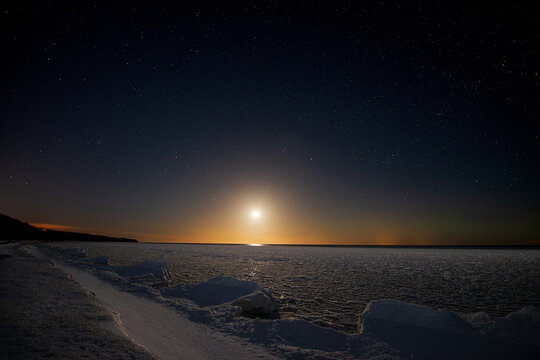 Seashore covered with ice under a starry sky with moonset