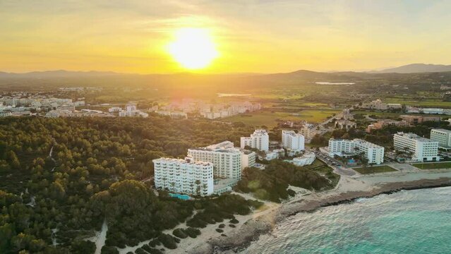 Susnet over Cala Millor, flying above the sea, hotels, and mountains in the background, drone footage, aerial video