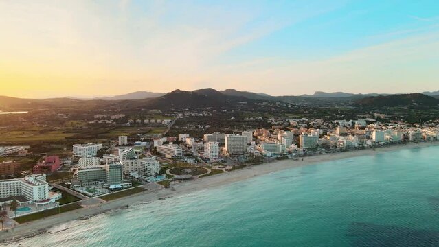 Susnet over Cala Millor, flying above the sea, hotels, and mountains in the background, drone footage, aerial video