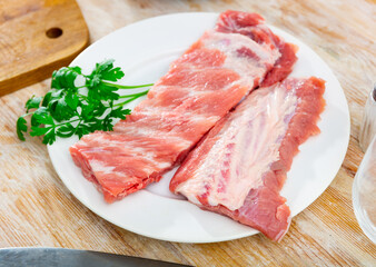 Raw meaty pork ribs slabs on plate with fresh greens ready for cooking ..