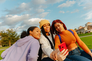 multiracial group of three teenage girl friends using a smartphone to take photos together. classmates and friendship. youth culture and technology