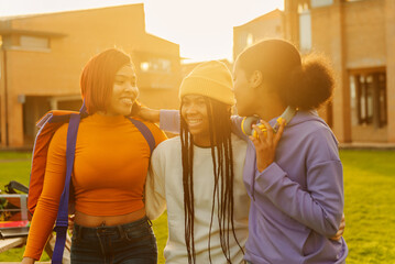 multiracial group of young girls having fun leaving class on college campus. female friends laughing together at sunset. unity and friendship concept.