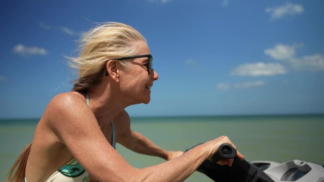 Closeup Of Pretty, Fit, Blonde Mature Senior Woman Happy And Laughing Driving A Jet Ski On The Water With Her Hair Blowing In The Wind.