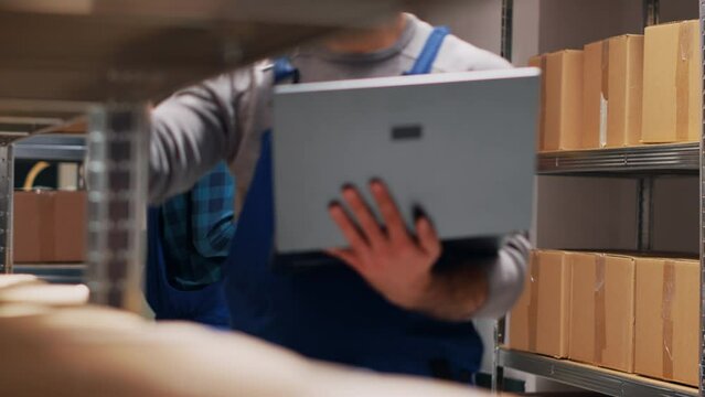 Caucasian worker holding laptop with inventory list, checking merchandise stock and planning order shipment. Male manager holding pc to do quality control for goods. Handheld shot.