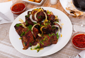 Oriental grilled pork meat shashlik with sliced onion rings on a white ceramic plate