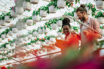 Multiracial couple of gardeners working in a greenhouse and using clipboard