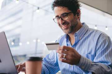 Middle-aged Latin man inserting his bank card into the laptop with a smile on his face. Copy space.