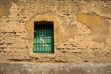 Fototapeta na wymiar Ventana con barrotes en pared de adobe, pared rural de casa de campo en pueblo
