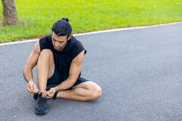 Caucasian man in sportswear tying running shoe laces during jogging exercise at park in summer morning. Healthy guy athlete enjoy outdoor lifestyle sport training fitness workout running in the city
