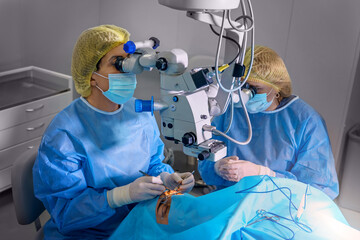 Blepharoplasty plastic surgery. Rejuvenation and modification of the area around the eyes. Plastic surgeon and nurses doing eyelid surgery on a female patient using a microscope