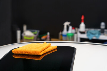 Automotive detailing studio. Close-up of an orange rag lies on the roof of a car. - obrazy, fototapety, plakaty