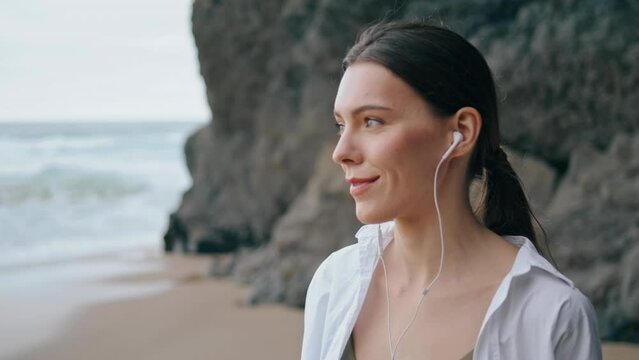 Woman answering phone headphones standing beach in front sandy hill close up.