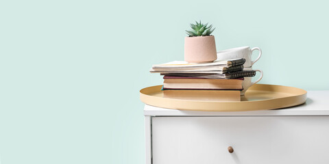 Tray with books, notebooks, succulent plant and cups on chest of drawers in room