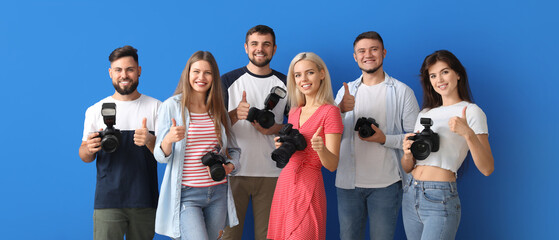 Group of happy young photographers showing thumb-up gesture on blue background