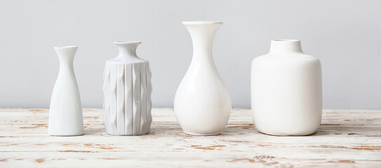 Fototapeta na wymiar Different white vases on wooden table against light background