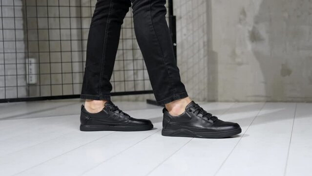 Unrecognized man in black jeans and leather sneakers showing moonwalk. Stylish male footwear demonstration in studio.