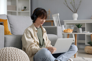 Male student in headphones using laptop at home