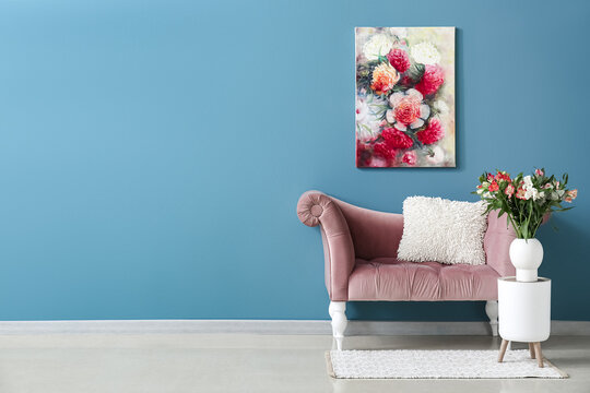 Vase with alstroemeria flowers on stool, cozy armchair and beautiful painting near blue wall