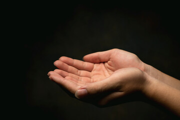 Close-up hands of woman praying on dark background.