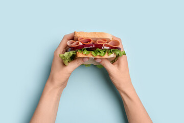 Female hands holding delicious ham sandwich on blue background
