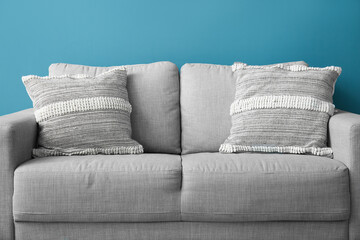 Stylish decorative pillows on cozy grey sofa near blue wall